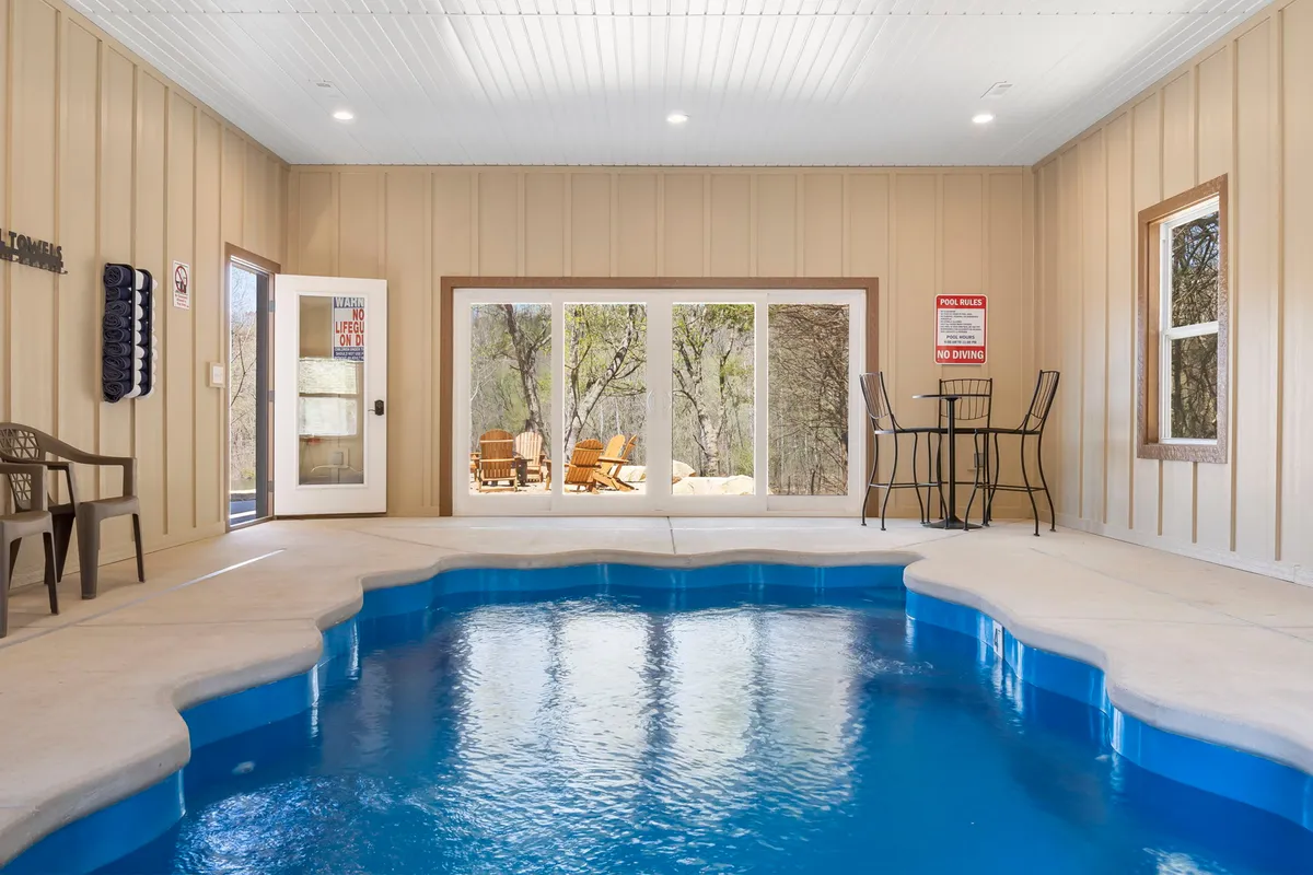 The image showcases a stunning private indoor swimming pool flooded with natural light from expansive windows, a stylish bar table perfect for gathering, and a seamless view of the inviting outdoor seating area. The serene setting hints at both relaxation and fun with space for group activities.
