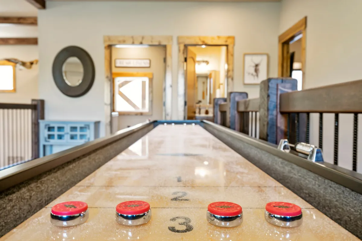 A shuffleboard table is the star of this inviting room, accompanied by stylish furniture and wall art. The setting feels social and vibrant, with clear sightlines to adjoining spaces, suggesting easy flow between activities. The mood is friendly and full of anticipation for competitive fun.