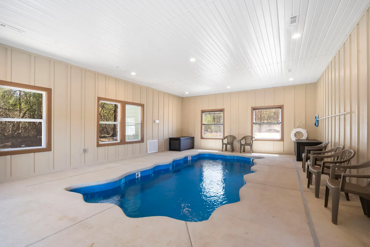 An inviting indoor pool area featuring a sparkling pool surrounded by comfortable lounge seating and large windows that let in natural light. The space is spacious and well-lit, offering both a relaxing and vibrant atmosphere for group gatherings or solo swims.