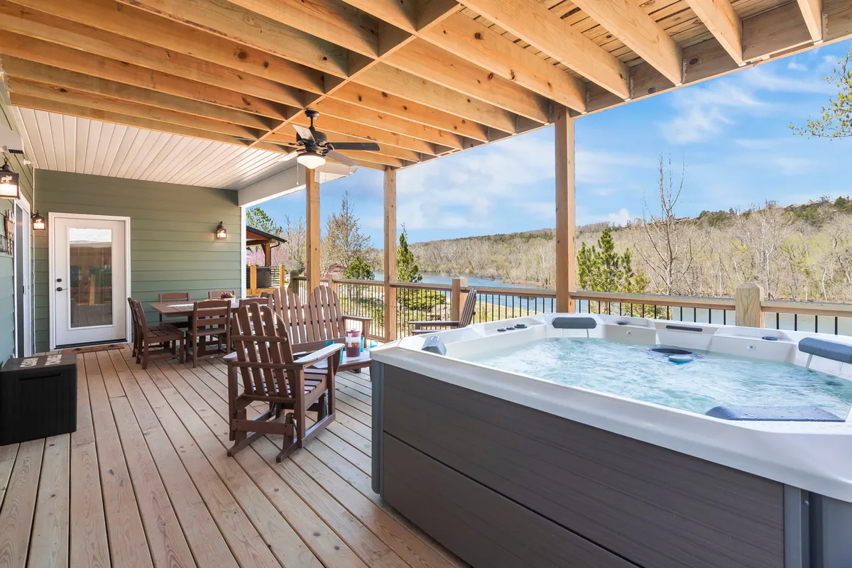 An exterior deck area with a bubbling hot tub, an adjoining dining area, and a breathtaking view of the lake. The wooden deck and cozy seating invite guests to relax and unwind while enjoying the scenery.