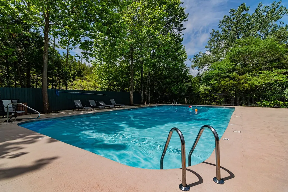 This image presents a sparkling outdoor swimming pool surrounded by lounge chairs and lush greenery, creating an inviting atmosphere for both relaxation and play. The pool deck offers plenty of space for families to gather and enjoy time together under the sun or stars.