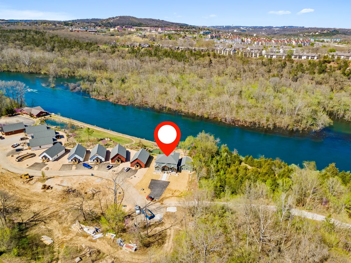 A scenic view of the river flanked by lush trees and several newly constructed homes along the bank. The inviting landscape hints at boating, fishing, and nature walks, with the water winding through the resort area.