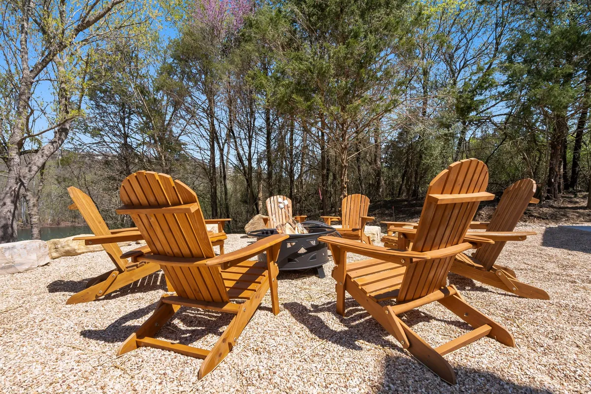 A cozy fire pit setting surrounded by classic Adirondack chairs, nestled amongst tall trees. The scene invites guests to unwind, roast marshmallows, and share stories as the sun sets and stars emerge.