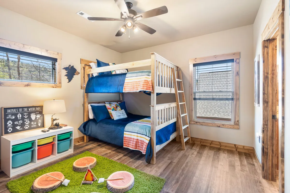 A cheerful custom bunk room with a bunk bed, colorful bedding, a green rug for play, a small lamp, and a storage unit. The setting feels playful and family-friendly, perfect for kids’ sleepovers and creative activities.